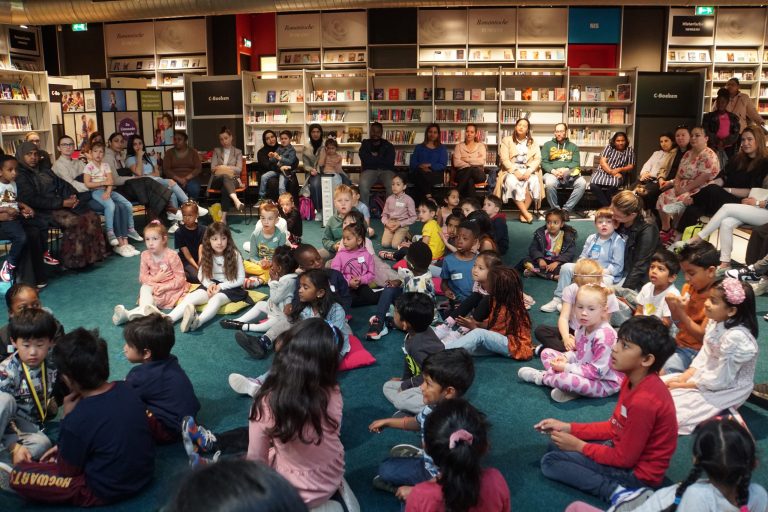 Kinderen zitten in een groepje en luisteren naar een verhaal in de bibliotheek.