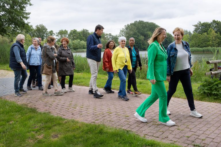 Groep mensen wandelt in Natuurpark Lelystad langs het water. Ze praten en hebben plezier.